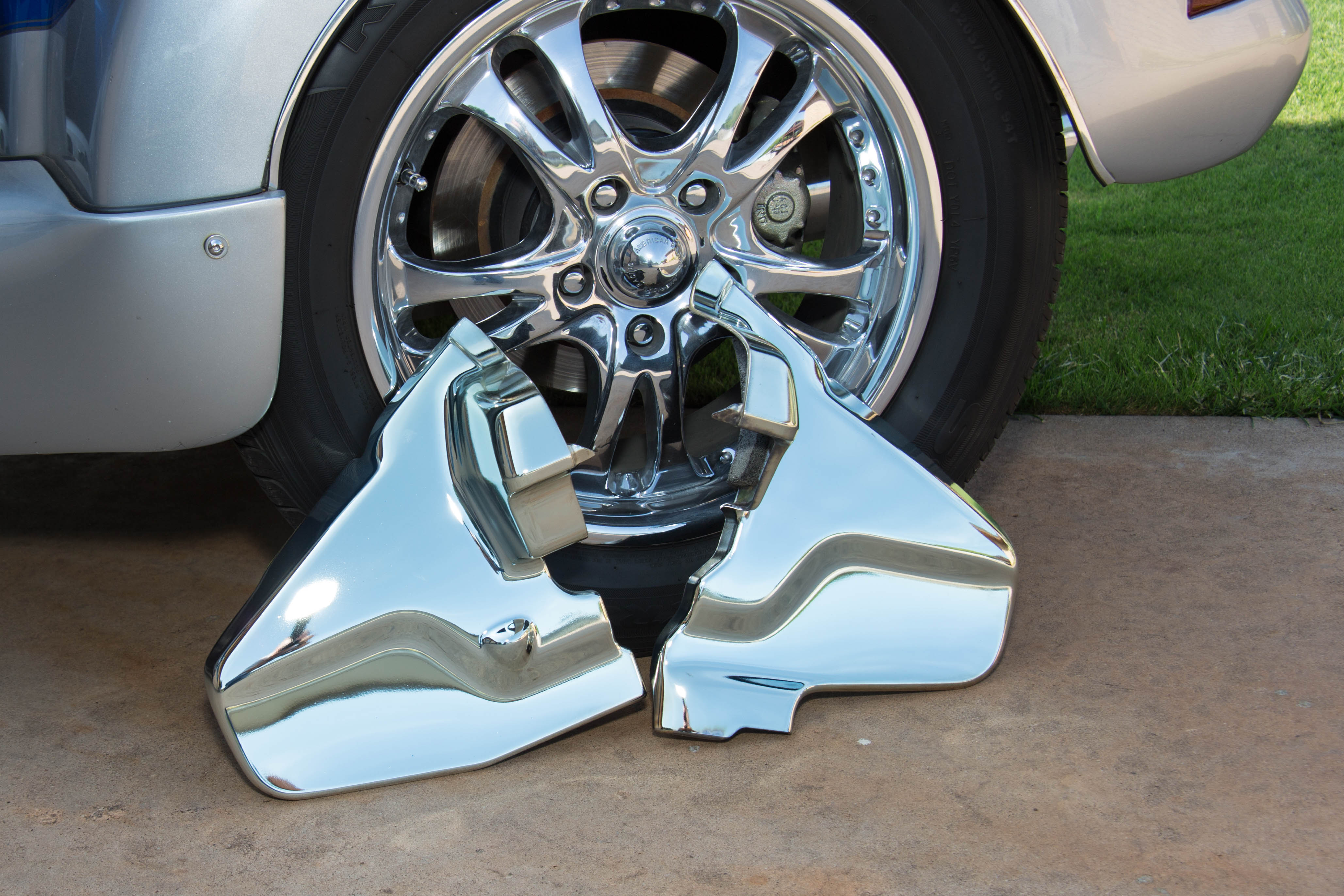 Two side covers of Goldwing trike spray chromed in front of a chromed tire rim showing similarity in chrome tone