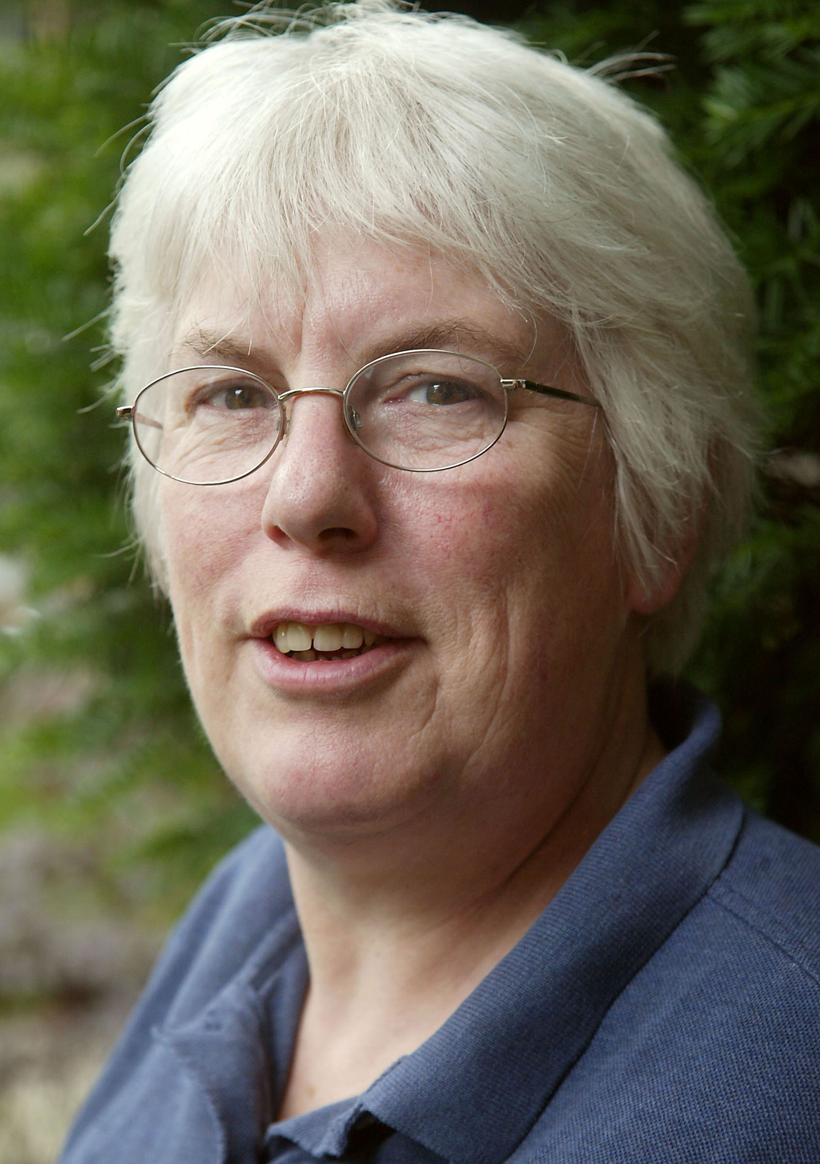 Headshot of Sarah King, an older white woman with short white hair, glasses and a deep blue polo shirt. She is smiling gently