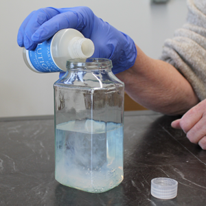 Pouring silver into a glass jar with tap water showing cloudiness, signaling impure water
