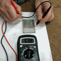 two hands holding prongs of electrical conductivity meter showing conductivity of silvered glass